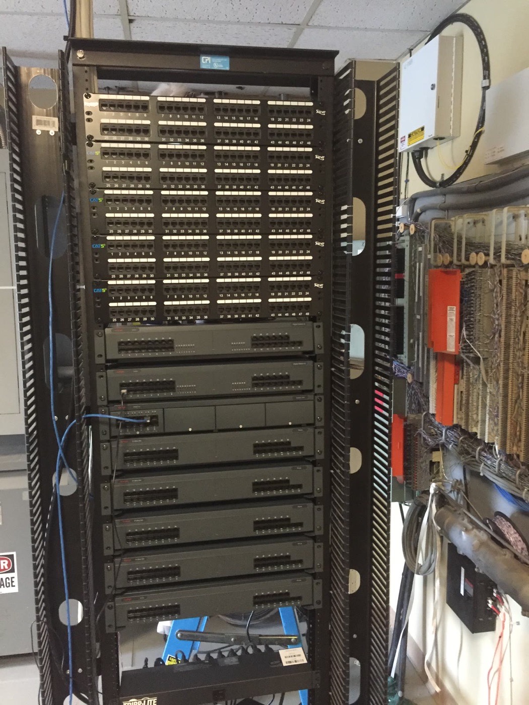 Full-height rack of certified Cat5e patch panels beside a legacy voice system