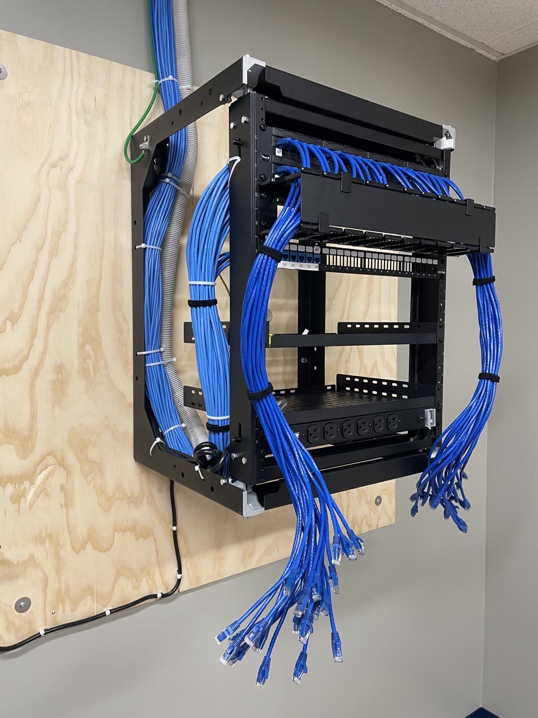 Comm1data wall-mount rack build with velcro-dressed Cat6 harnesses on a plywood backboard